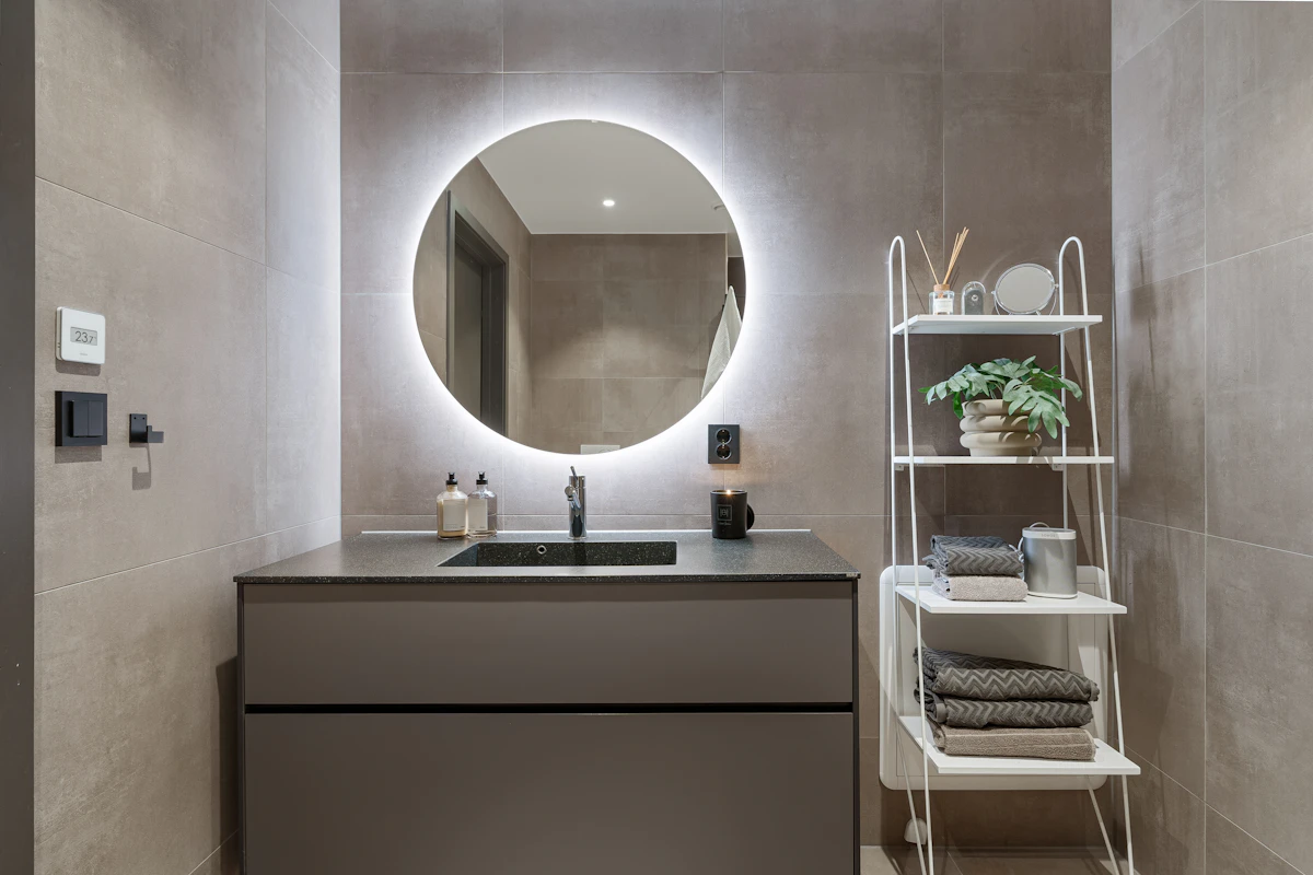 Small bathroom with vanity, round mirror, and narrow open shelving