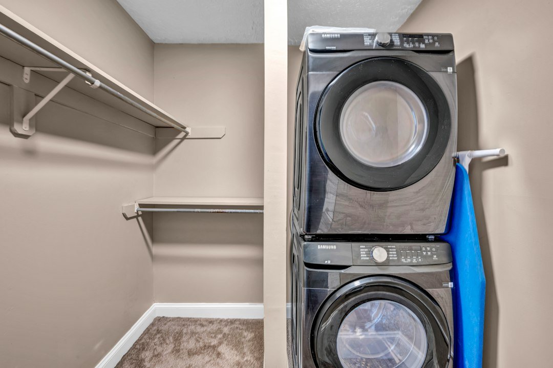 Stacked washer and dryer beside wire shelving in a compact apartment laundry closet