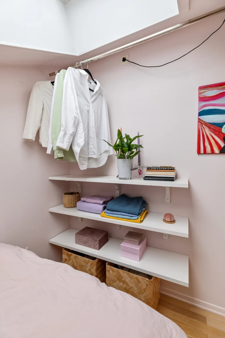 Small bedroom with open wall shelves holding folded clothes and baskets