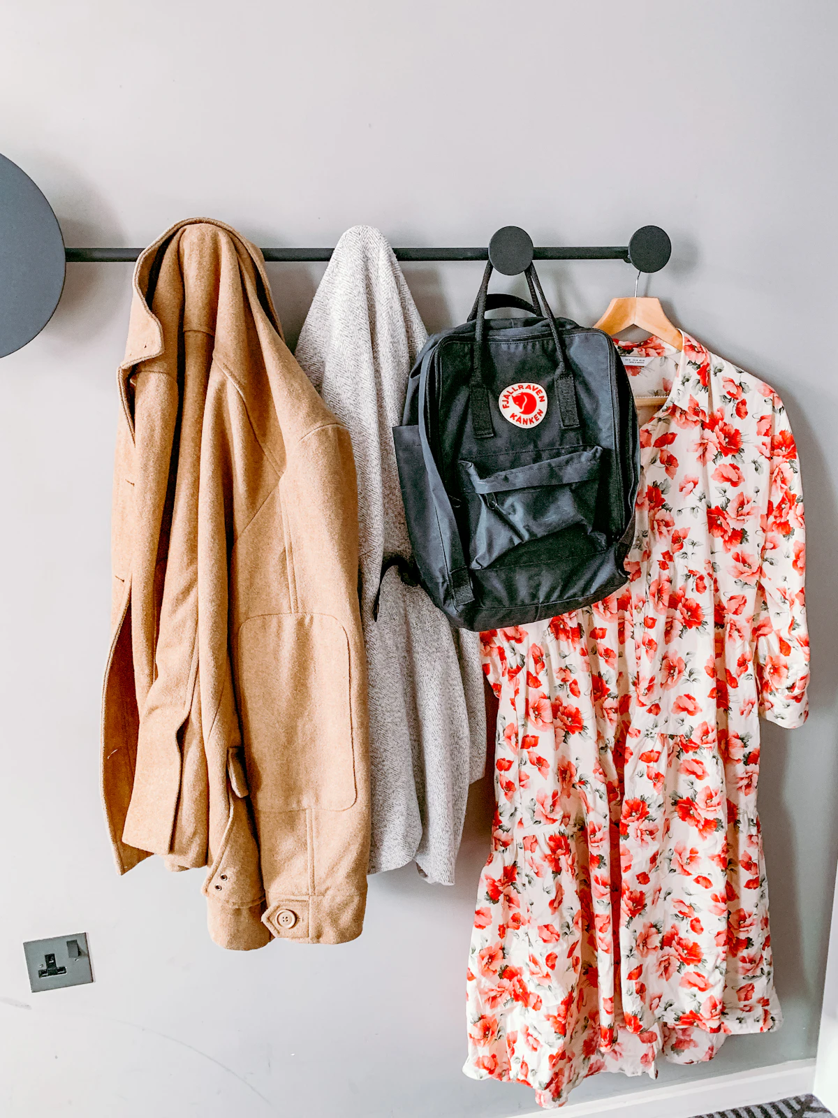 Coats, clothing and a backpack hanging from a wall-mounted rack