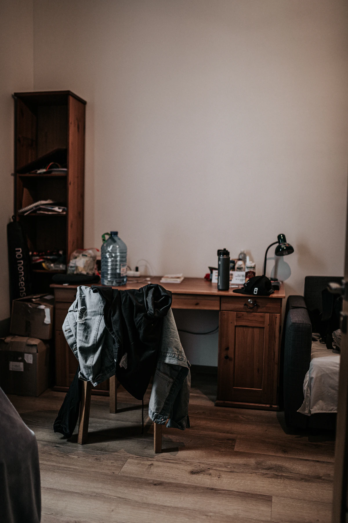 Bedroom desk and narrow shelving crowded with clothing and personal items