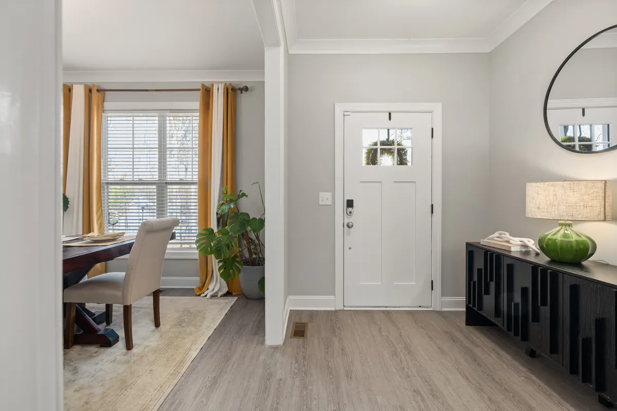 Front door opening beside a living and dining area with a narrow cabinet and mirror