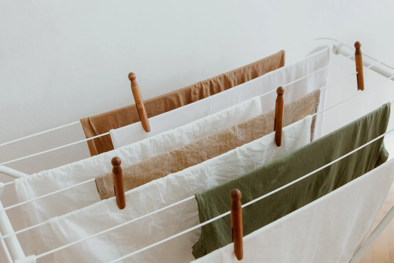 Light-colored laundry on a compact rack near a window, illustrating small space laundry drying solutions