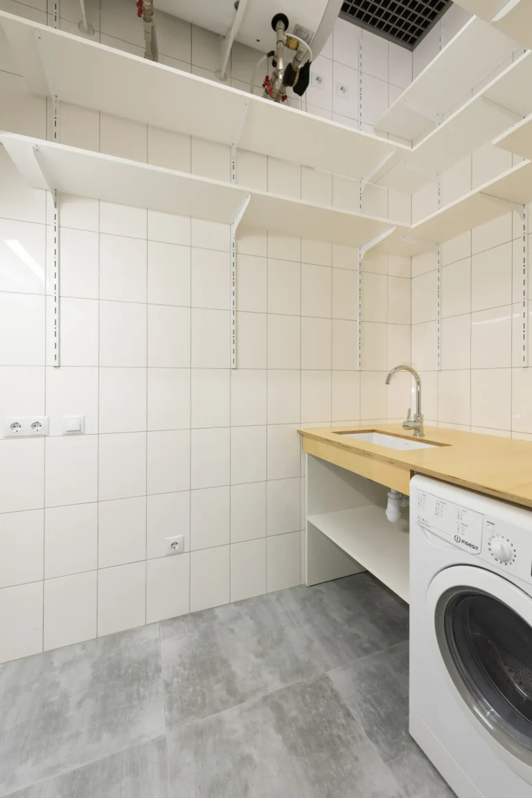 Laundry room organization without cabinets using open white shelves above a utility sink beside a washer