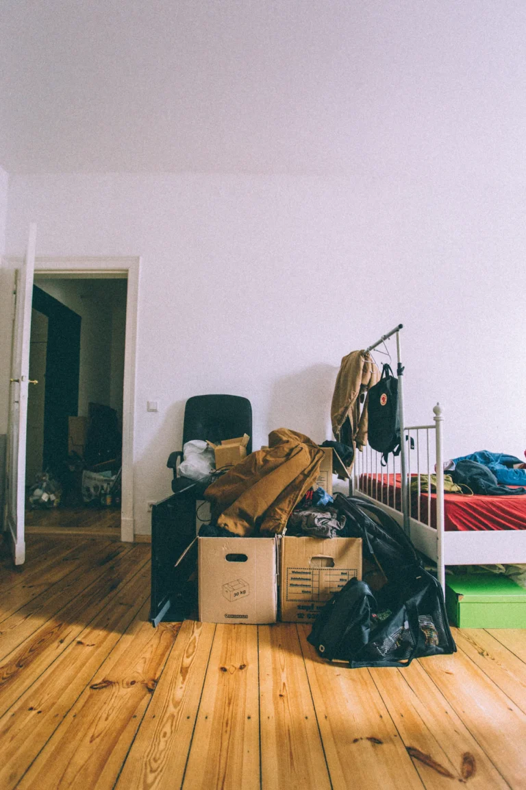 Small bedroom floor crowded with boxes, bags and loose belongings
