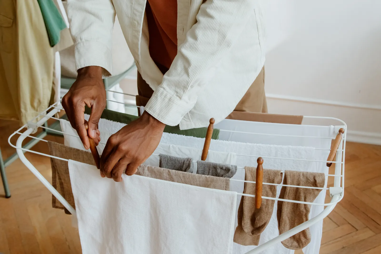 Person arranging clean laundry with space between garments on an indoor drying rack