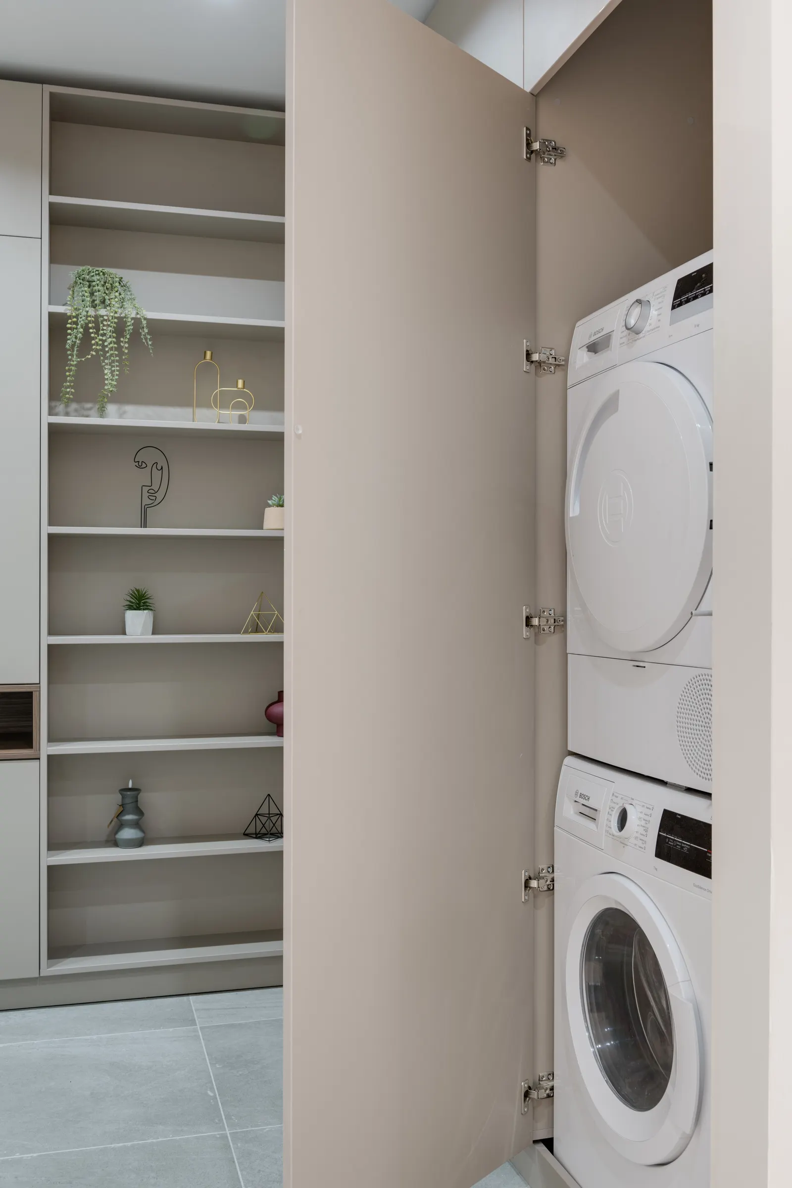 Small laundry closet organization with stacked front-loading machines and shelving beside the appliances