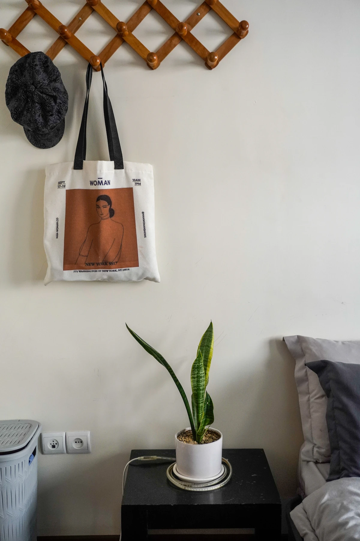 Accordion wall hooks holding a hat and tote bag beside a bed